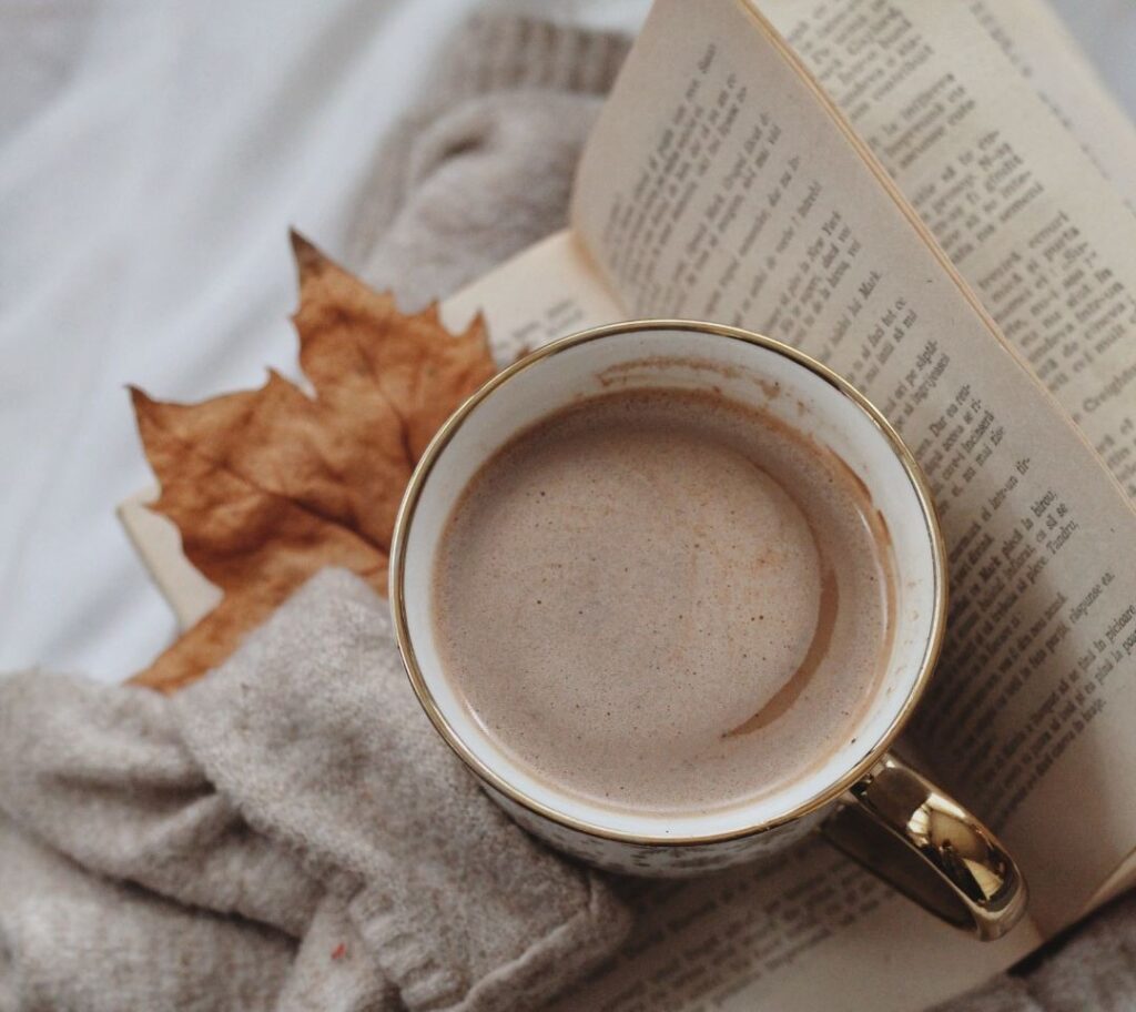 A warm drink, an open book, fall leaves, and a cozy sweater. 