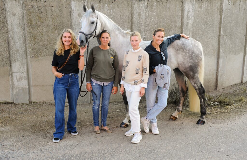 Get the galop team, 4 girls / women with a white / grey horse with spots. The women are touching the horse wearing horse / get the galop clothes. 